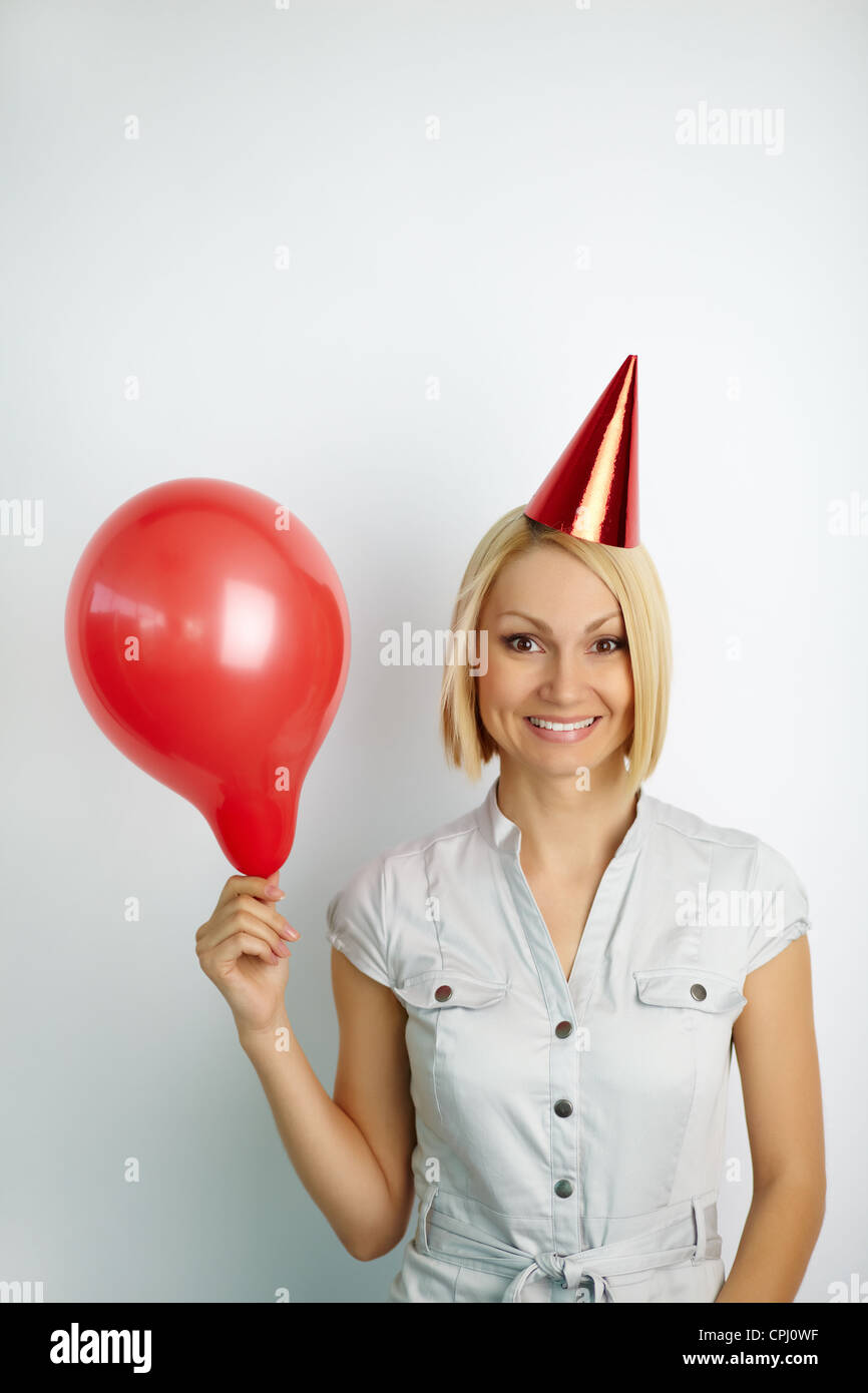 Portrait of a pretty blonde with red balloon wearing birthday cap Stock Photo