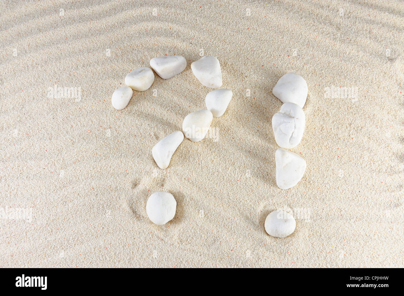 Question and exclamation mark arranged by stones with sand background Stock Photo