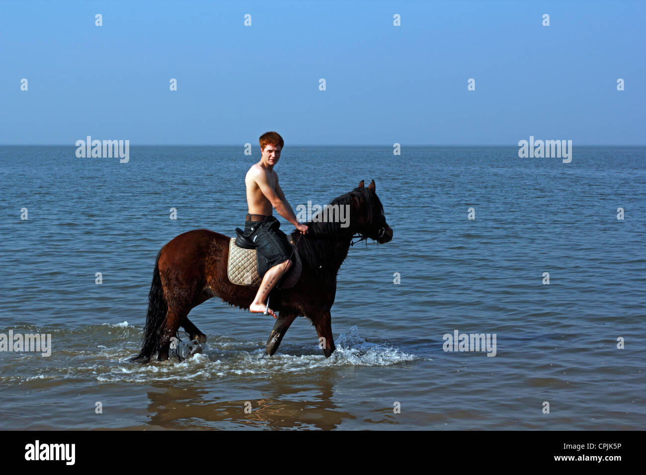 A young man rides his horse through the sea at Morecambe. Stock Photo