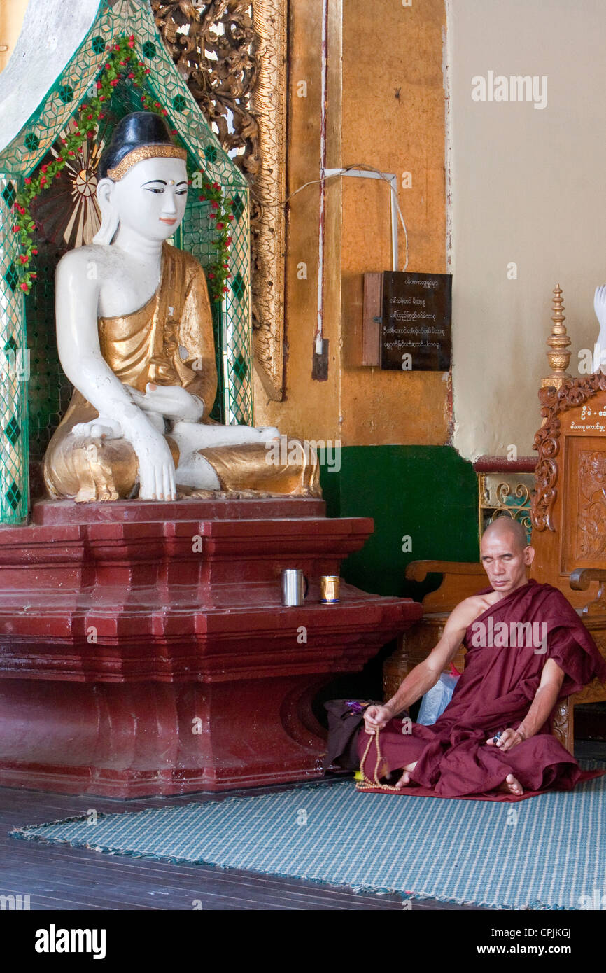 Buddhist Monk Praying Beside Buddha demonstrating mudras (hand gestures) of earth-touching (bhumisparsha) and wisdom (dhyana). Stock Photo