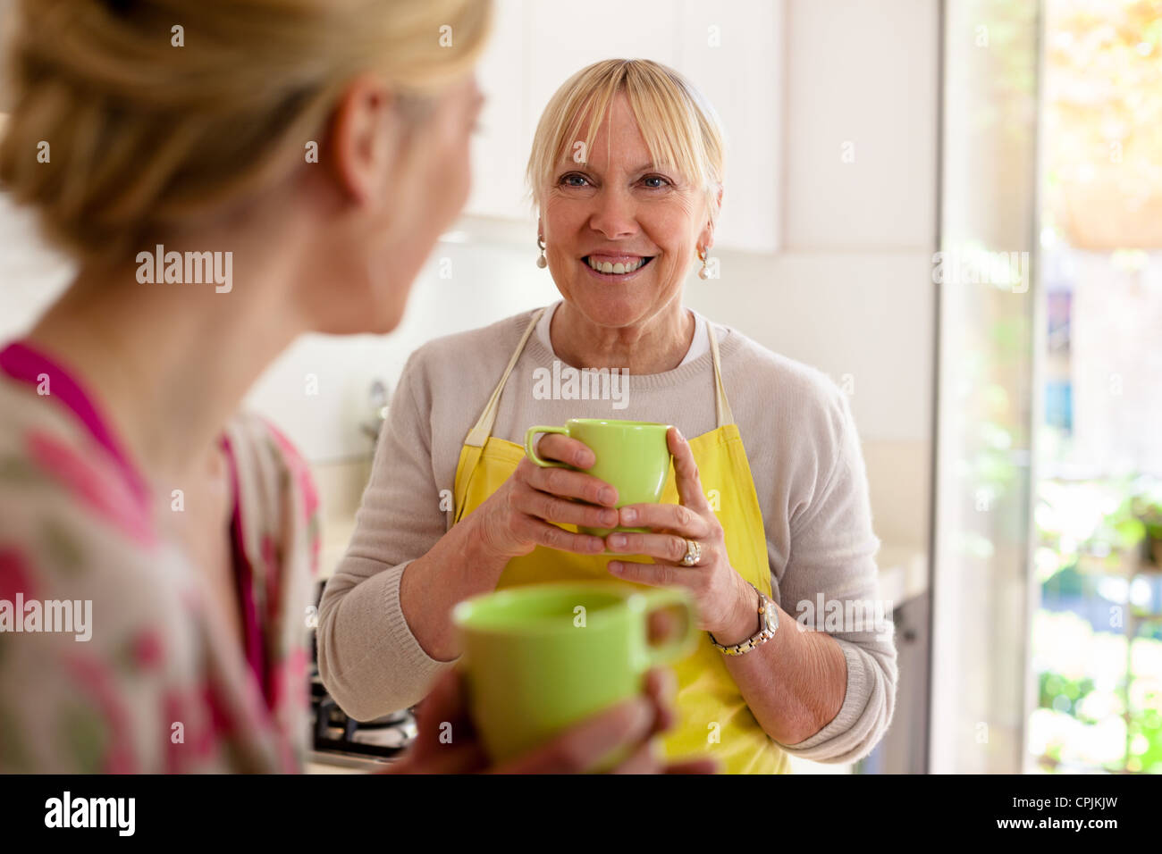 Happy women in home kitchen mom and daughter talking and drinking a