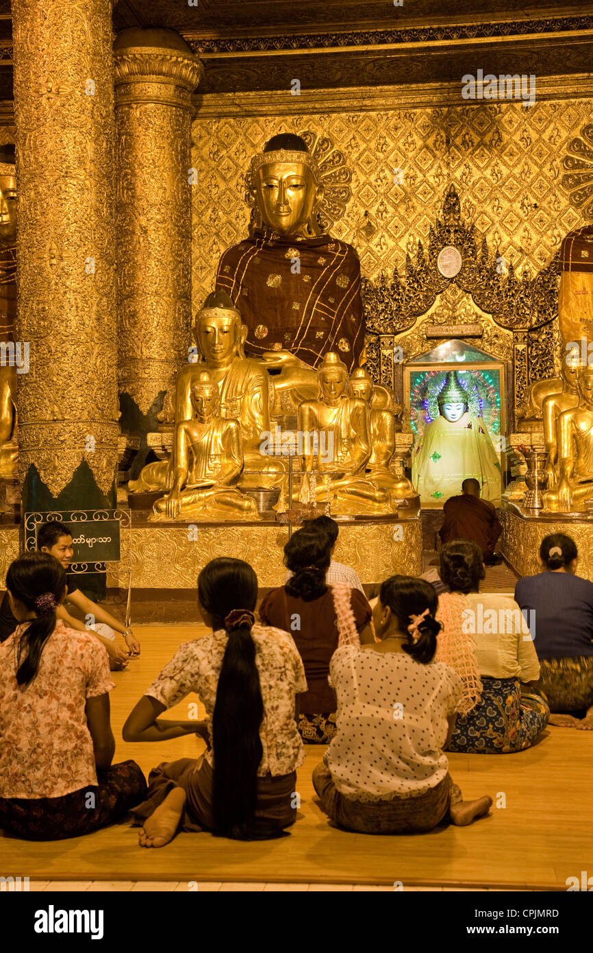 Myanmar, Burma. Shwedagon Pagoda, Yangon, Rangoon. Evening Lights Illuminate Worshipers Praying in a Buddhist Shrine. Stock Photo