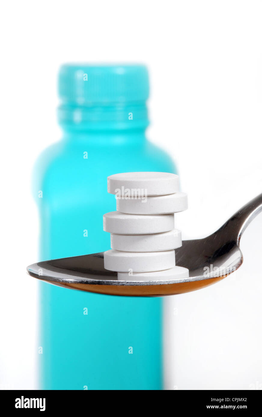 Antacid tablets on a spoon, a bottle of antacid blurred in the background Stock Photo