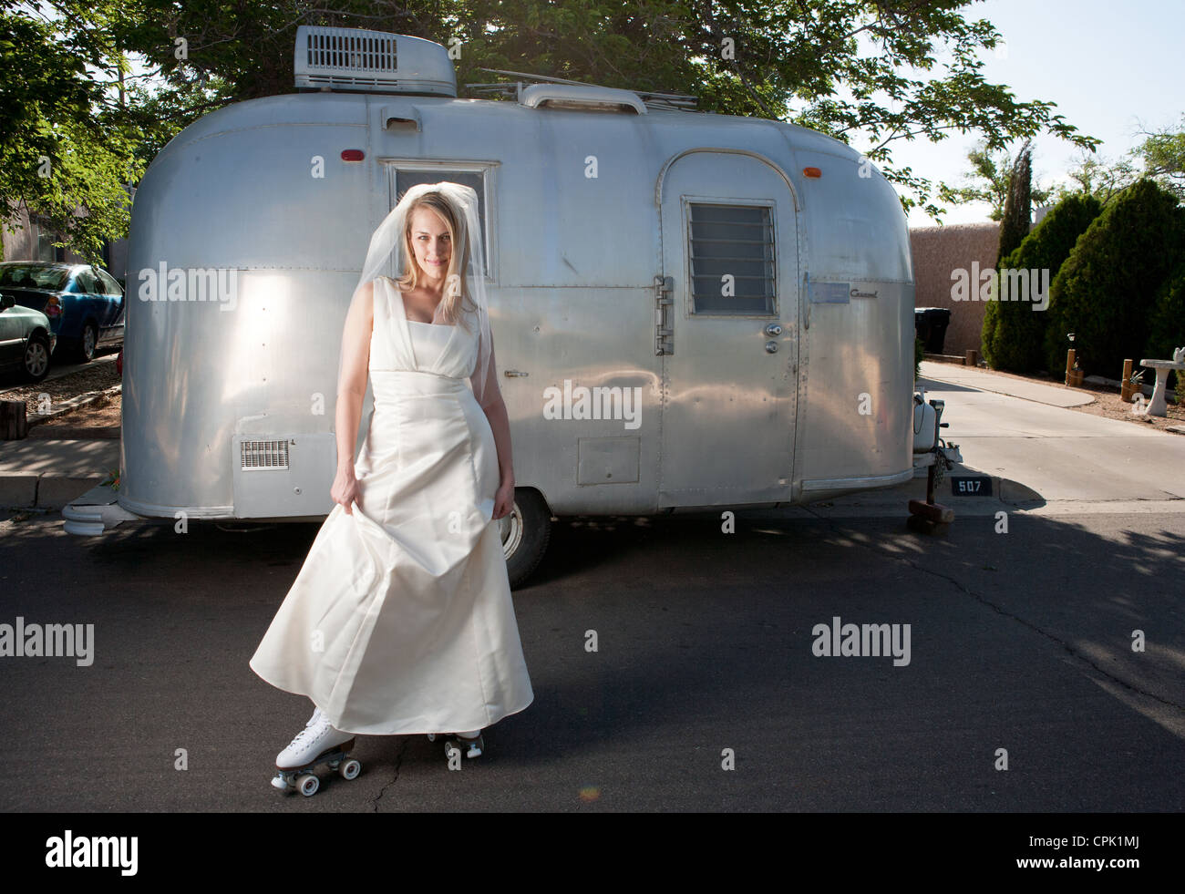 Bride wearing roller skates and standing in front of a trailer. Stock Photo