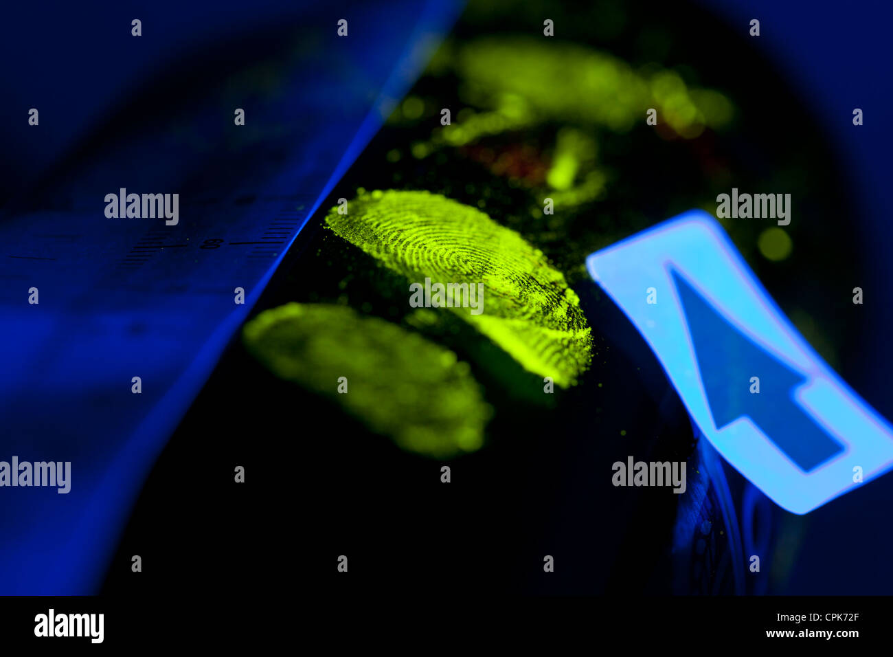 Crime scene fingerprint on object enhanced with ultraviolet dusting powder and photographed under ultraviolet light source by Crime Scene Investigator Stock Photo