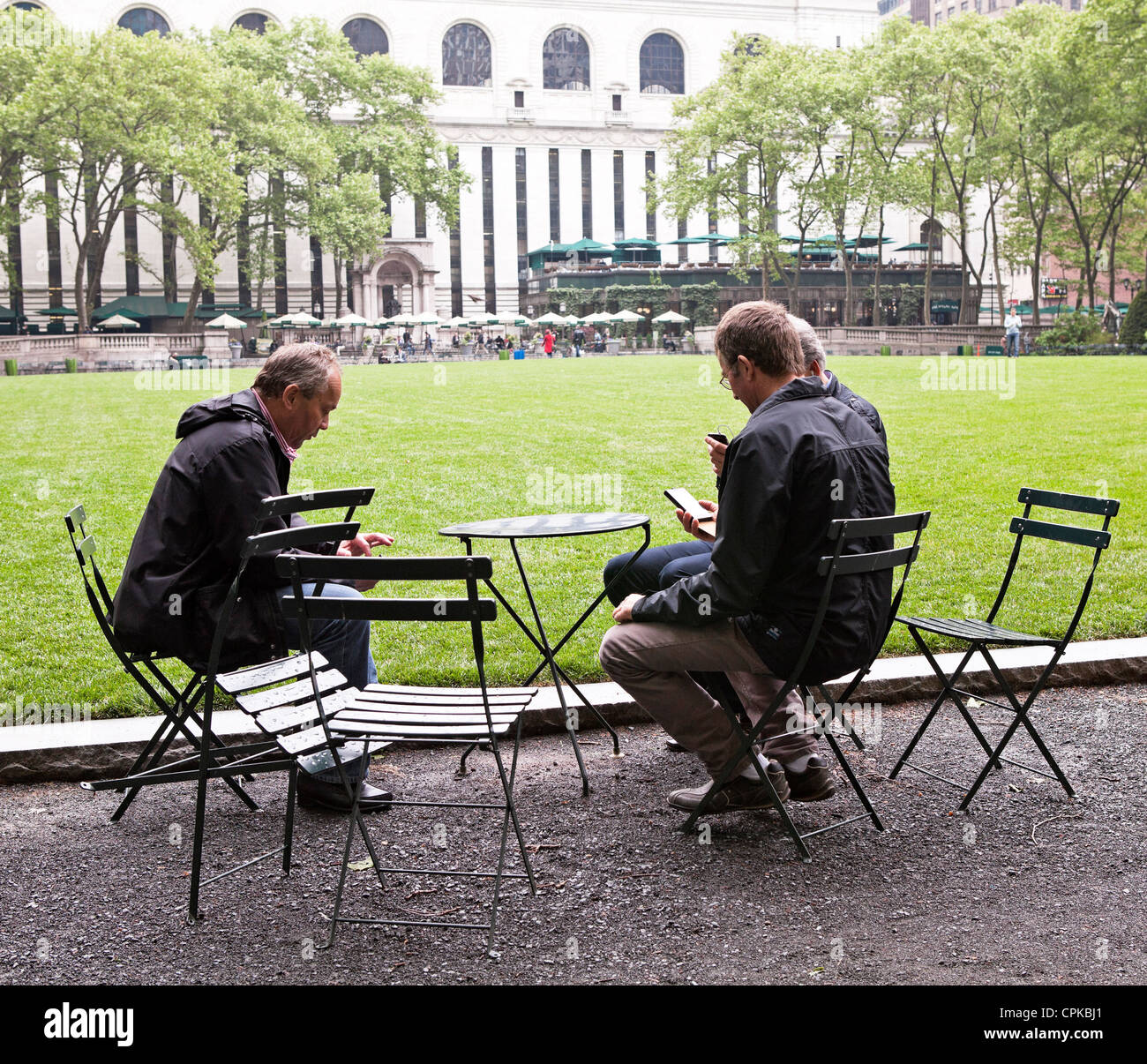 A group of men all look at their phones while sitting in Bryant Park in New York City. Stock Photo