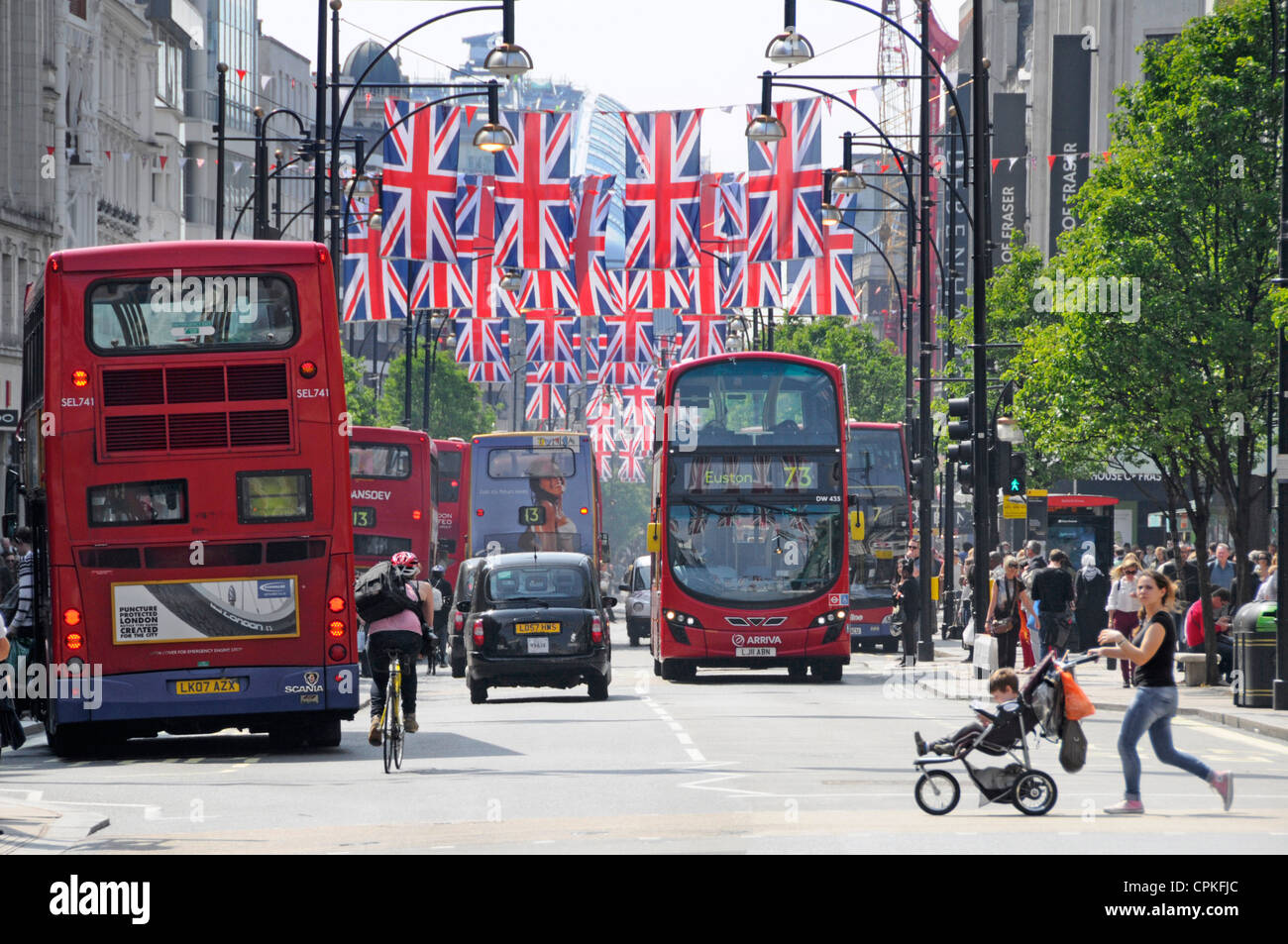Bus taxi & bike traffic in Oxford Street London West End England UK  Union Jacks for 2012 Olympic games & mother crossing road child in pushchair pram Stock Photo