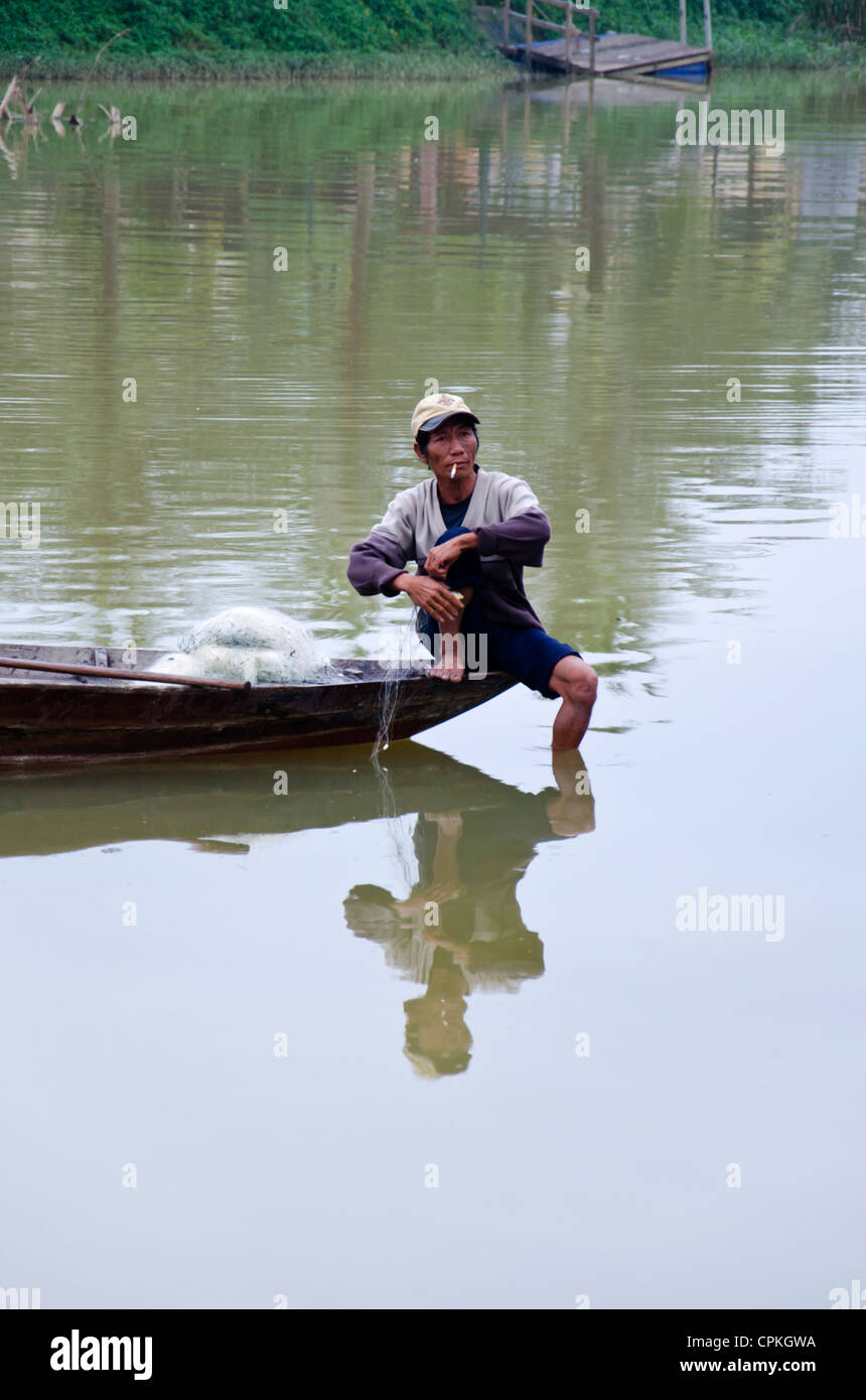 Fisherman in small boat pulling up fishnet. Sitting and balance on the boats edge and smoking Stock Photo
