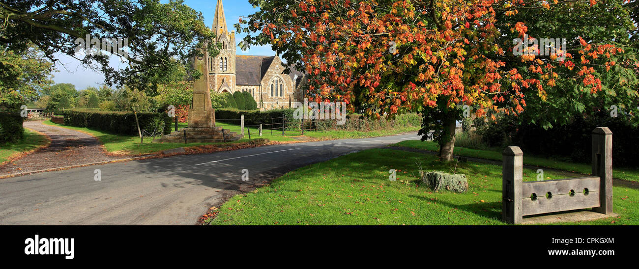 Wooden Stocks on the village green and St Johns Church, Lower Shuckburgh, Warwickshire, England; Britain; UK Stock Photo
