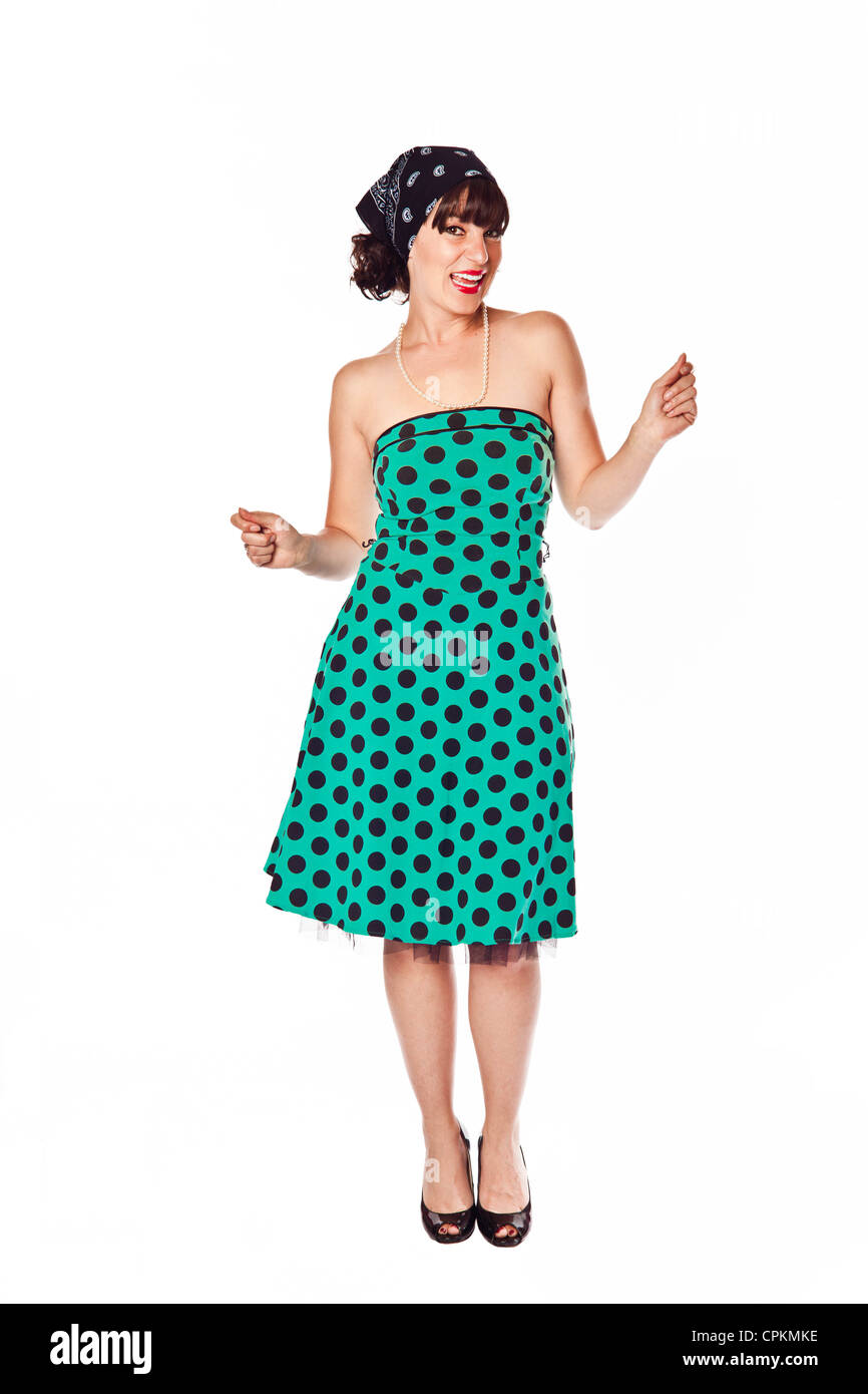 A brunette woman poses as a 1950's sock hopper in an aqua polka dot dress over a white background Stock Photo