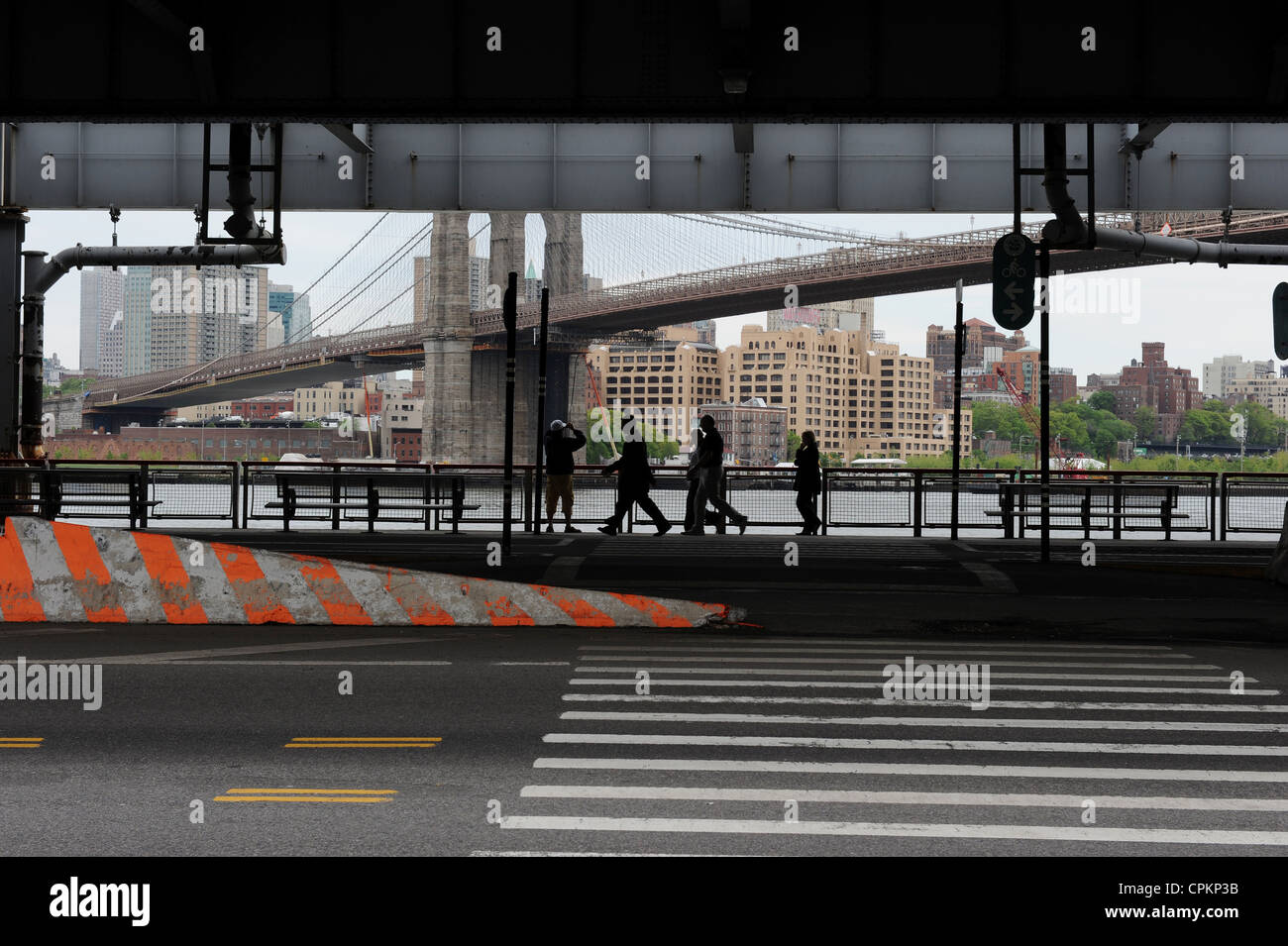 People walking under a bridge which shows Brooklyn Bridge in the distance, New York Stock Photo