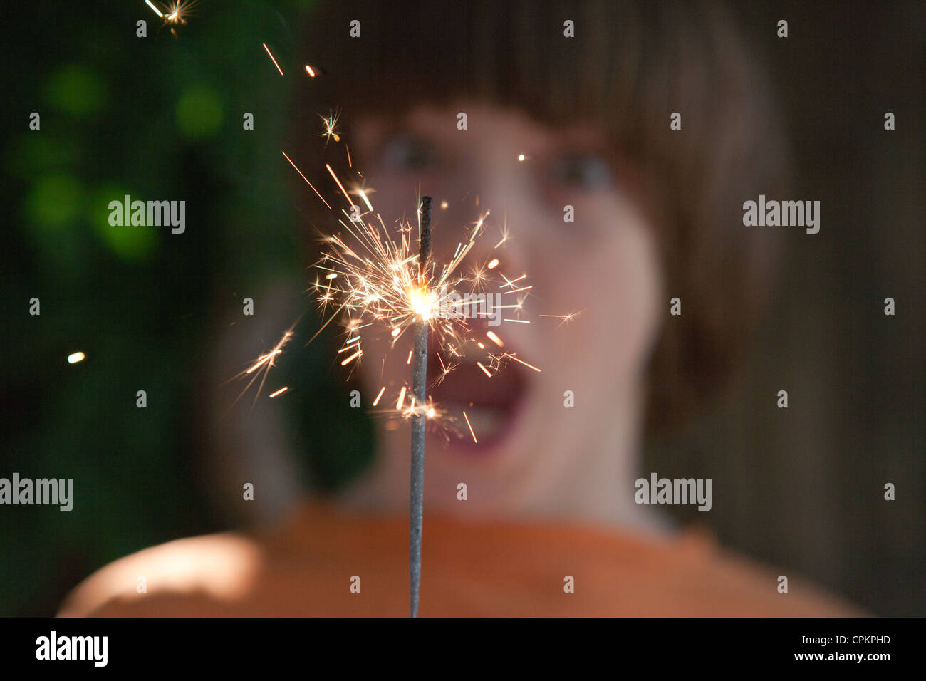 Close up of a boy holding a sparkler with surprised expression on his face. Stock Photo