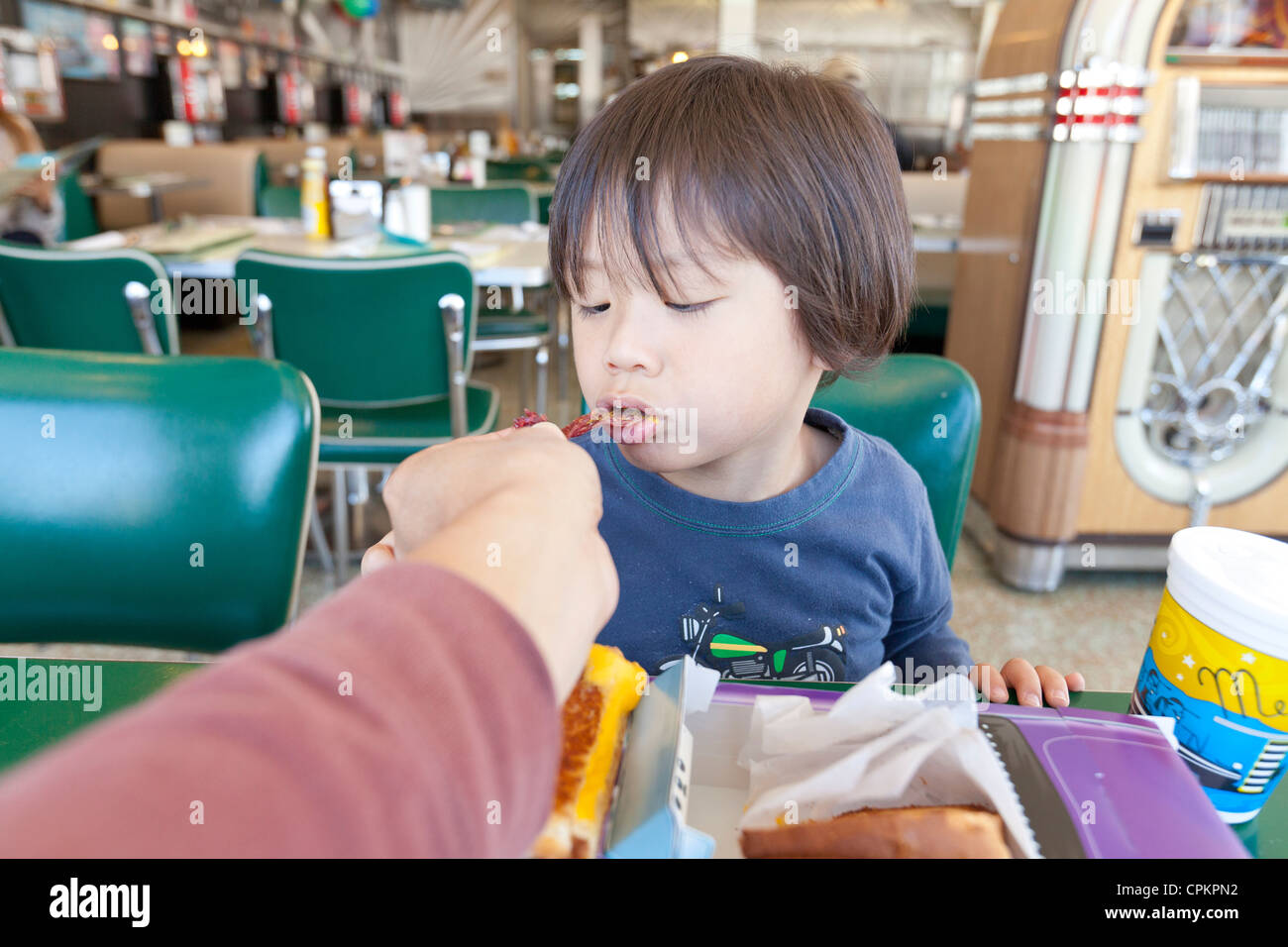 A young Asian boy being fed in a diner Stock Photo