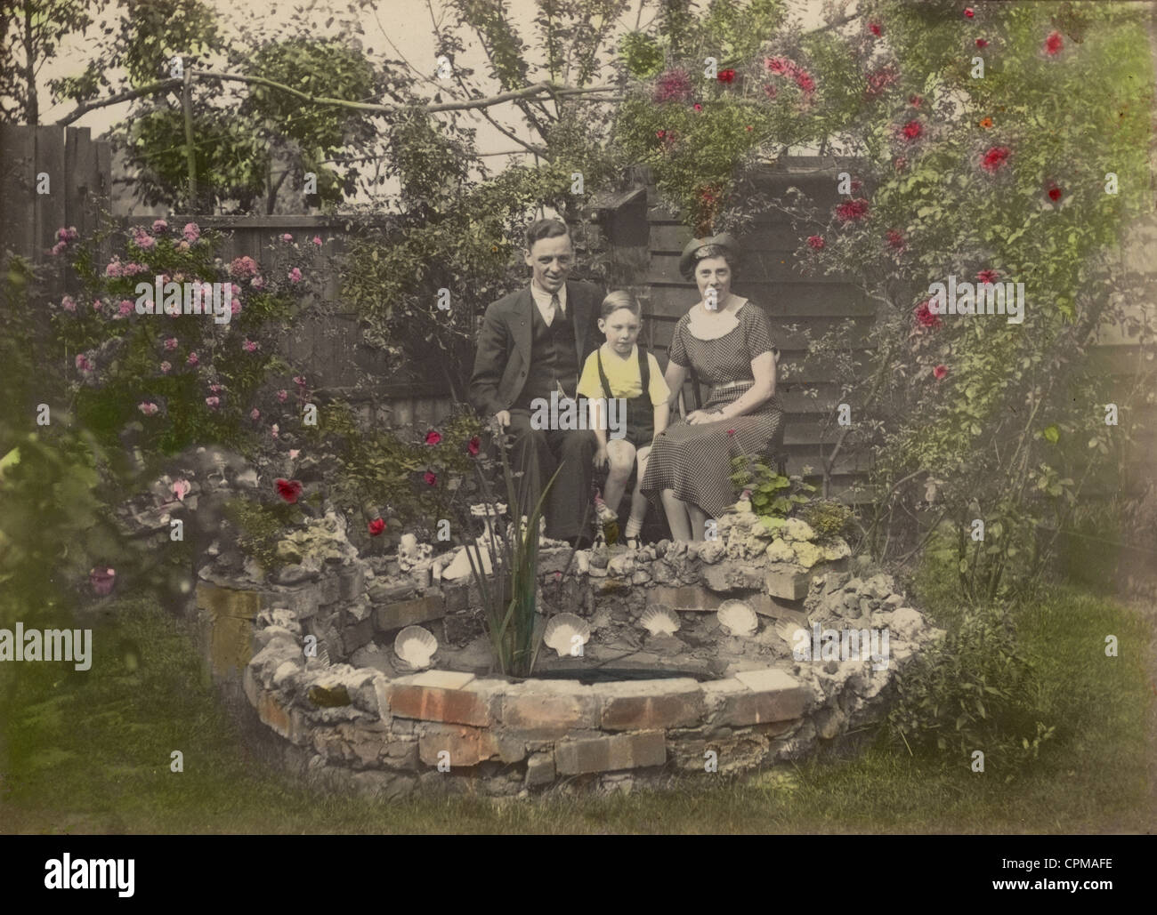 1920's original tinted black and white photograph of familydressed in their smart Sunday Best clothes,  posing proudly next to their garden pond in Southend-on-Sea, Essex, England, UK  circa 1922 Stock Photo