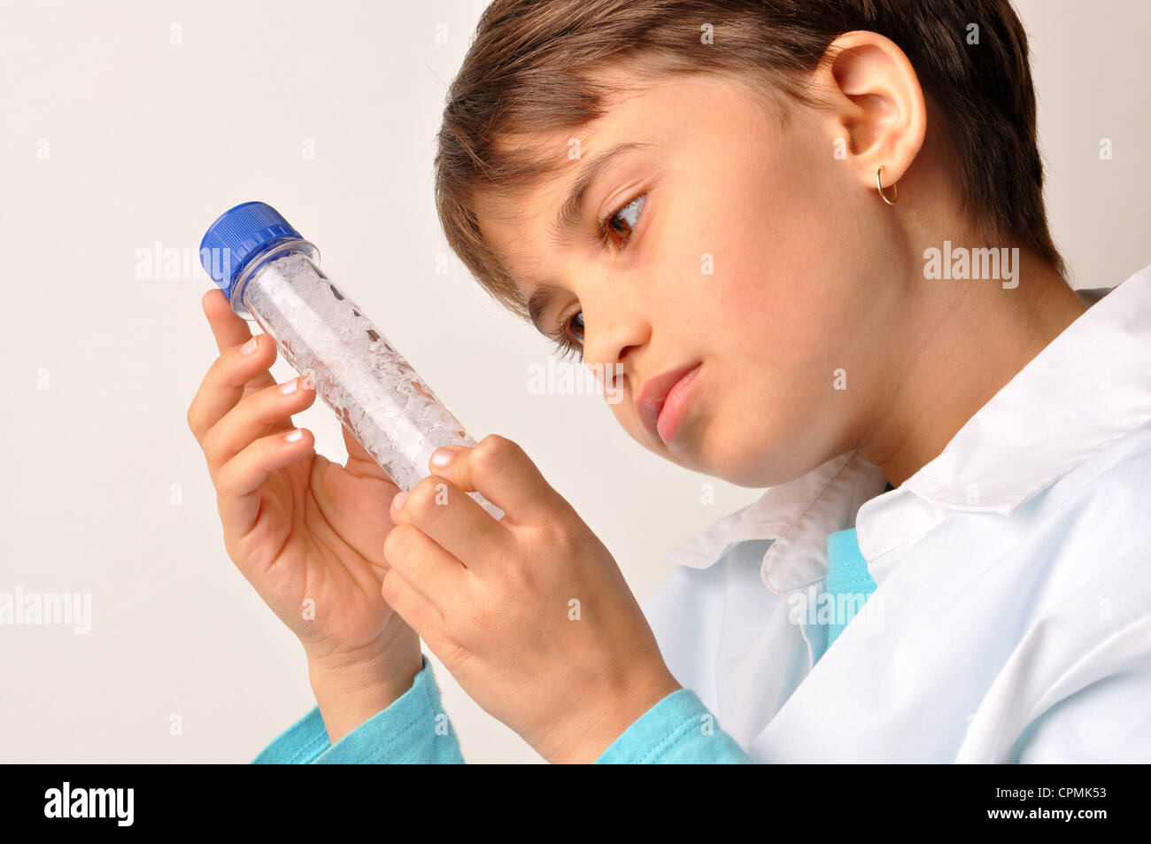 Science minded Adolescent bi-racial female gazing at Test Tube wearing white Lab coat Stock Photo