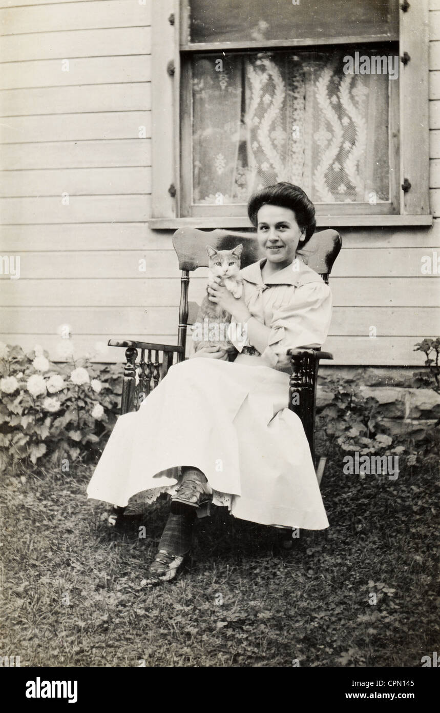 Young Girl in Rocking Chair Outdoors Holding a Cat Stock Photo