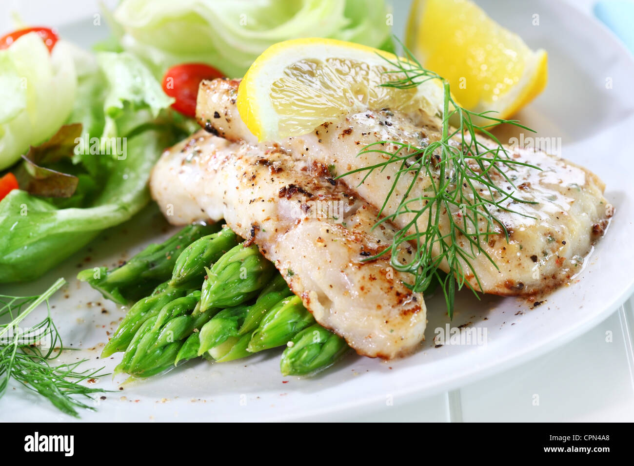 Delicious fried fish on green asparagus with salad Stock Photo
