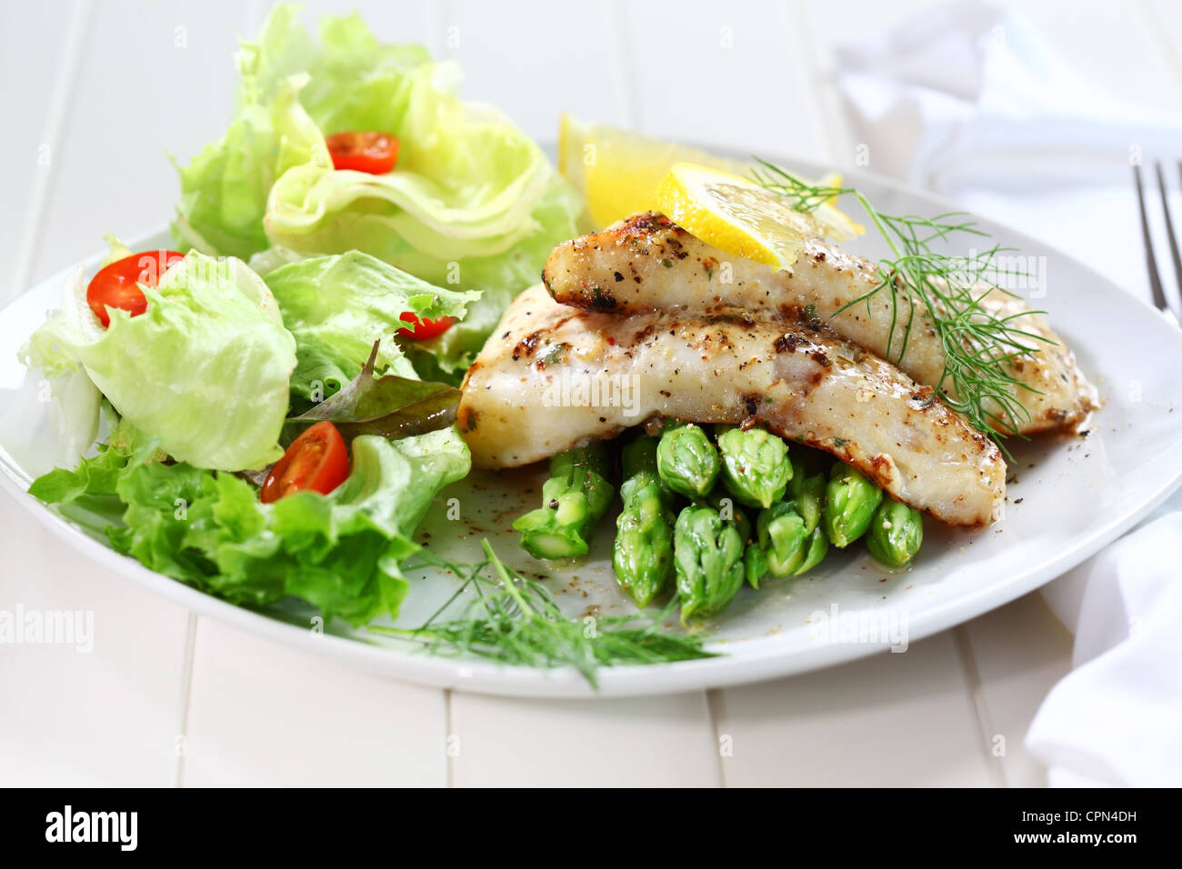 Delicious fried fish on green asparagus with salad Stock Photo
