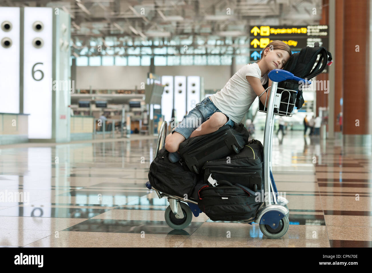 Girl resting on top of luggage cart in airport Stock Photo