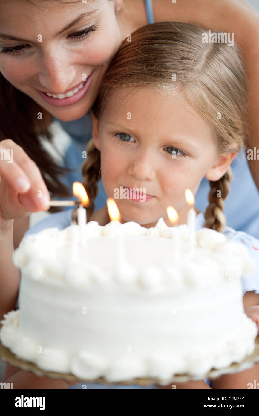 Girl watching as her mother lights candles on birthday cake Stock Photo