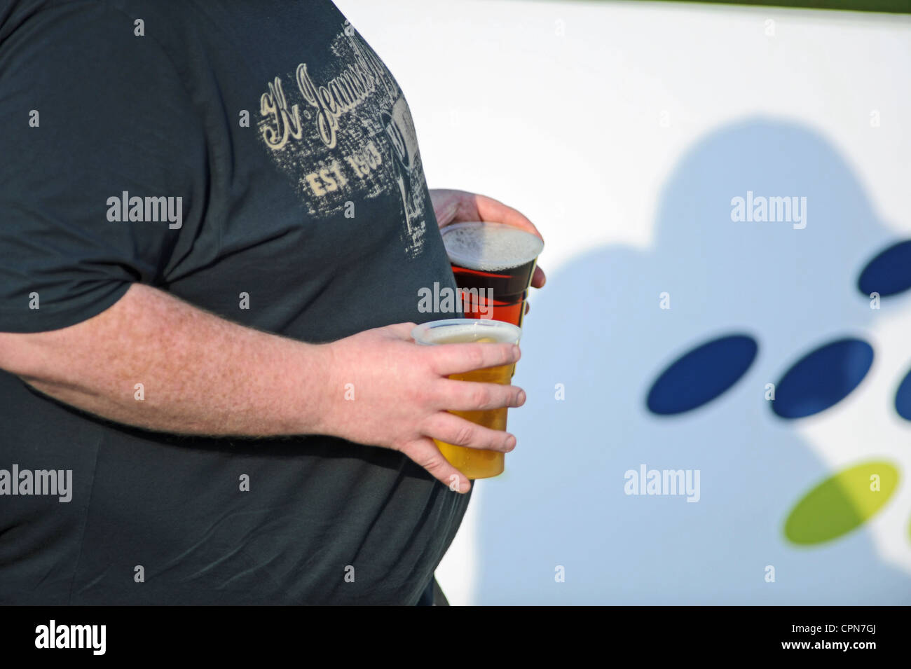 Man carrying pints of beer in plastic glasses in hot sunshine UK Stock Photo