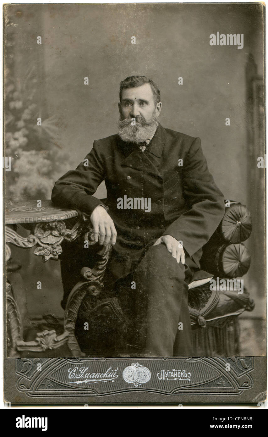 An antique photo shows man in a business suit with a mustache and beard, sitting in a chair at the table Stock Photo