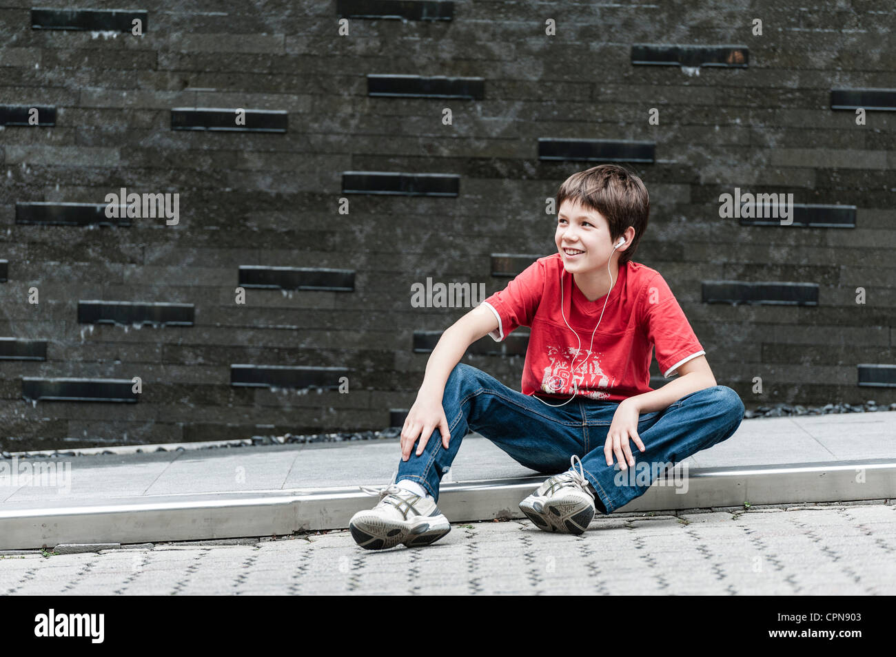 Boy sitting on sidewalk listening to music with earphones Stock Photo
