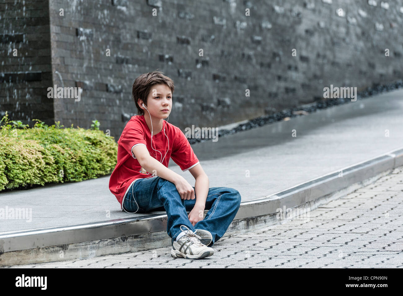 Boy sitting on sidewalk listening to music with earphones Stock Photo