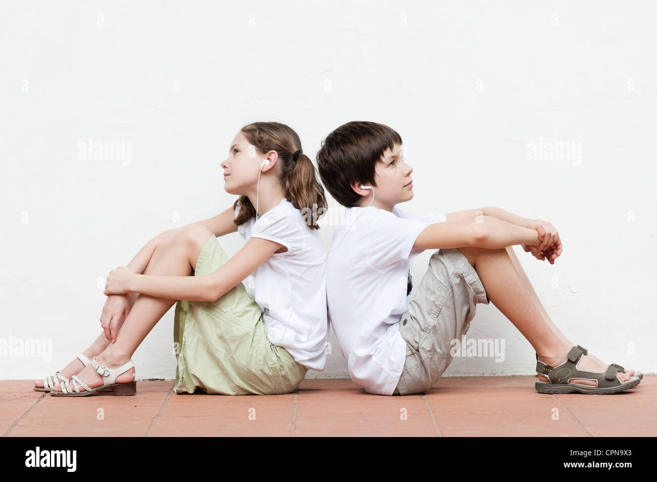 Boy and girl sitting back to back listening to music together Stock