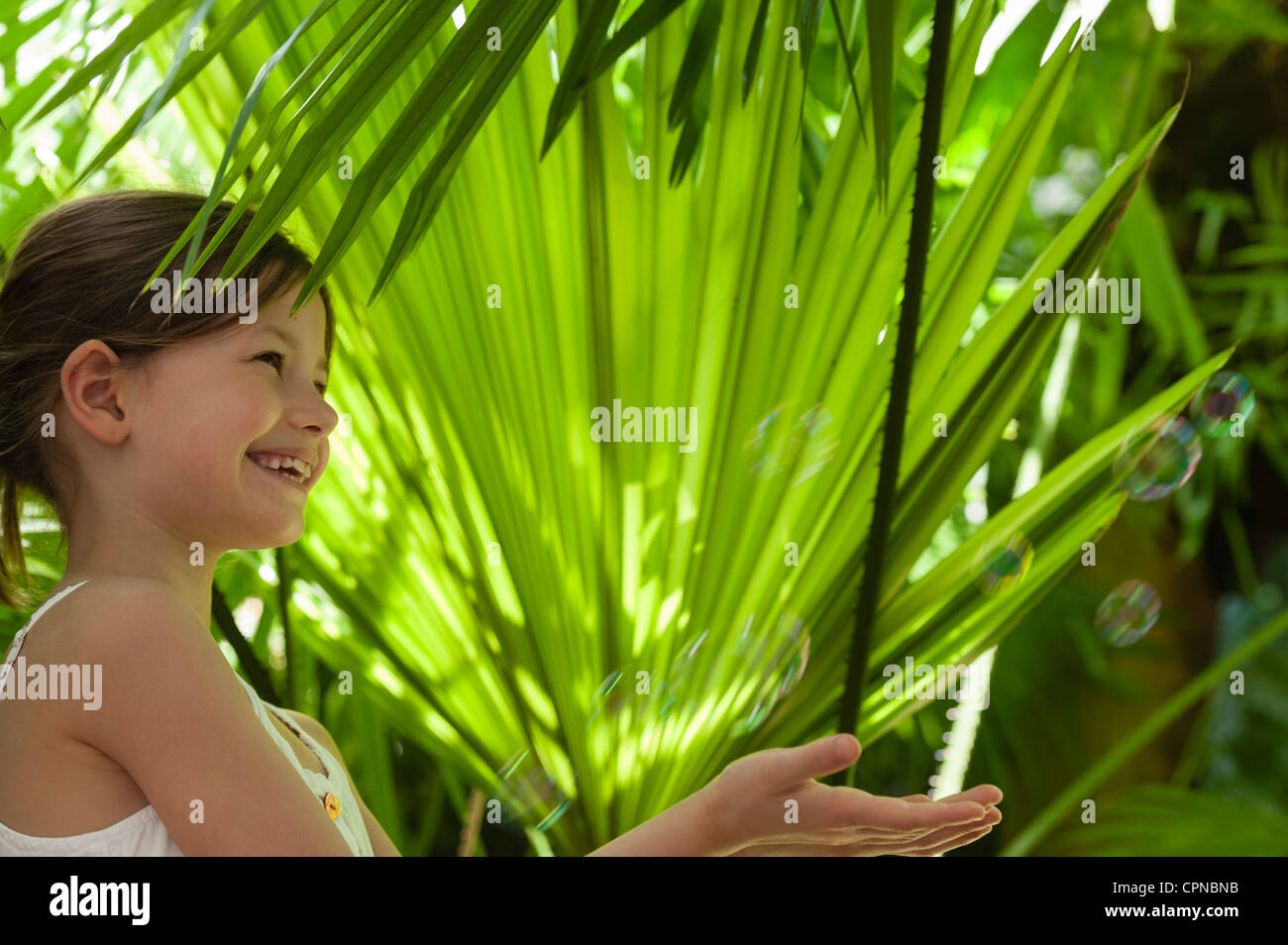 Girl playing with bubbles under palm leaves Stock Photo