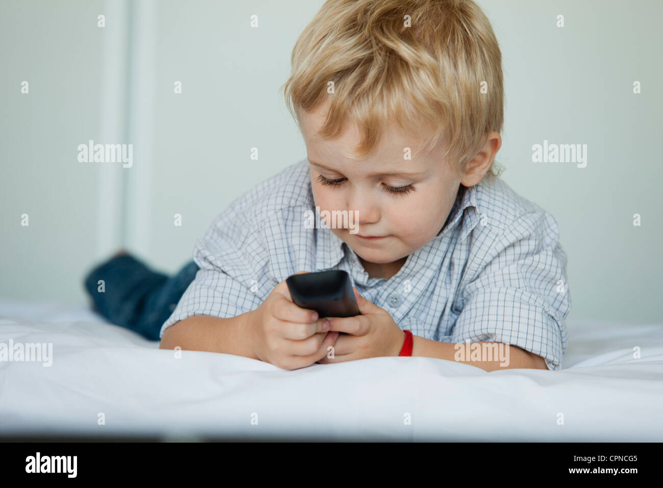 Little boy lying on bed holding cell phone Stock Photo - Alamy