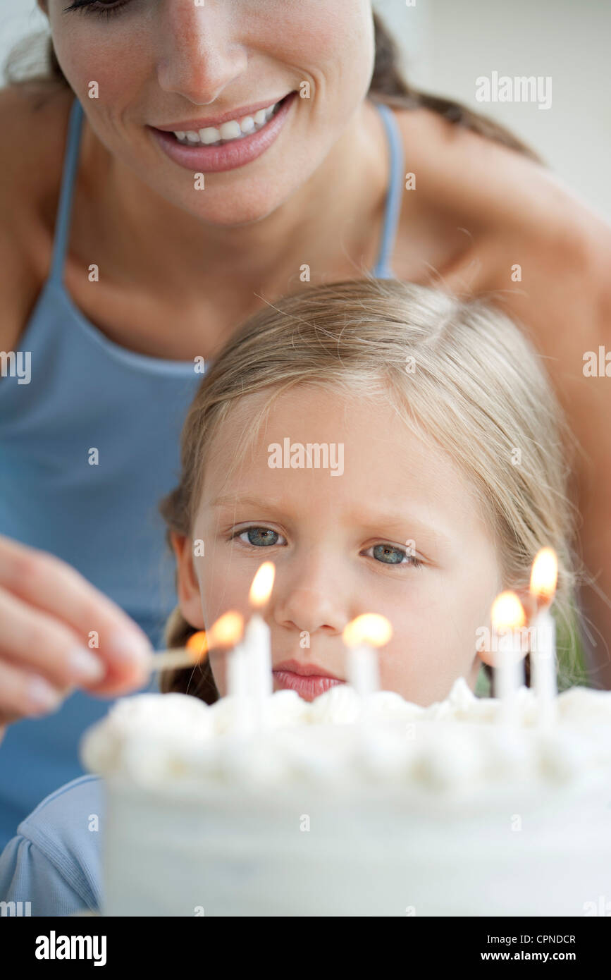 Girl watching as her mother lights candles on birthday cake Stock Photo