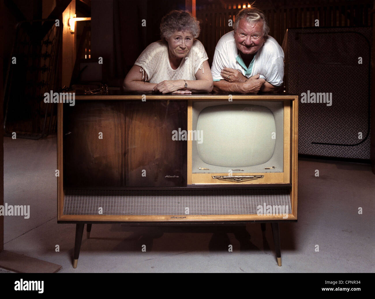broadcast,television,married couple with their dusted television cabinet Kuba Czardas from 1960 on the garret,Munich,Germany,couples,pensioner,pensioners,retired people,pensioner married couple,housetop find,TV device,television receiver,TV history,antiquarian appliance,technology,engineering,technologies,senior,seniors,antiquarian,60s,symbol image,symbolic,symbolical,outdated,out of date,out-of-date,television set,TV,television sets,TV sets,TVs,TV set,tube television,tube systems,tubes-receiver,home electronics,consumer el,Additional-Rights-Clearences-Not Available Stock Photo