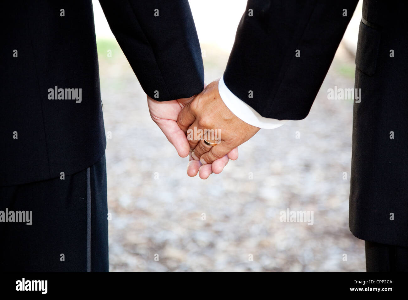 Closeup of a gay couple holding hands, wearing a wedding ring. Couple is a hispanic man and a caucasian man. Stock Photo