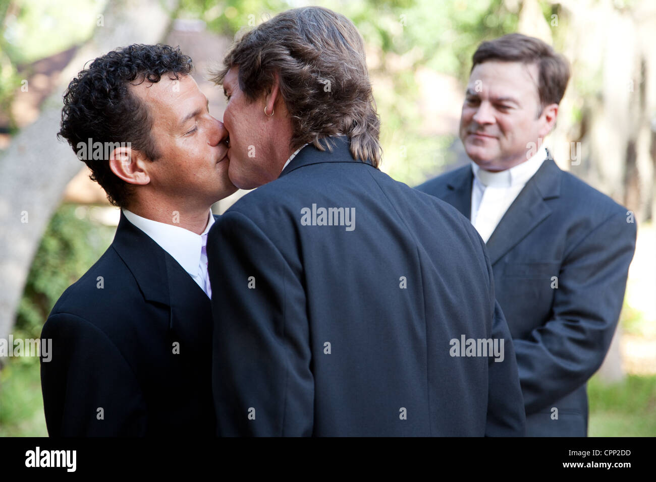 Wedding of handsome gay male couple. The grooms kiss as the minister looks on.  Stock Photo