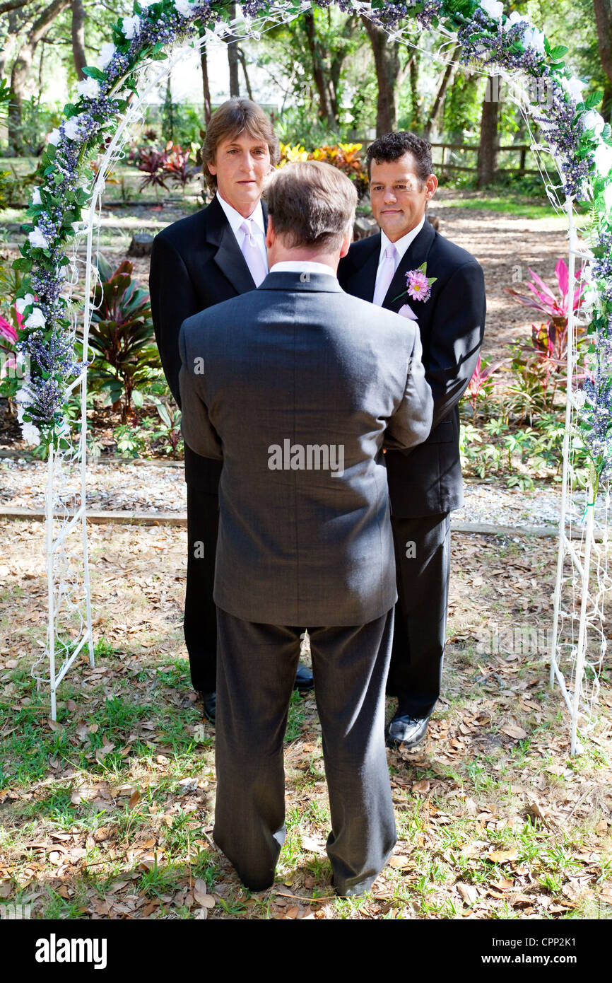 Gay male couple getting married in a beautiful garden setting underneath a floral archway.  Stock Photo