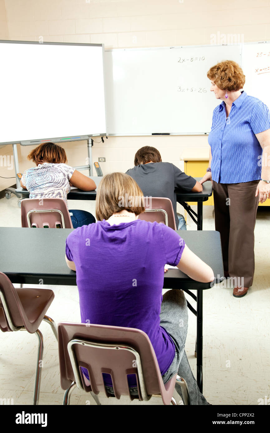 Students taking a standardized test as a teacher looks on to ensure no cheating.  Stock Photo