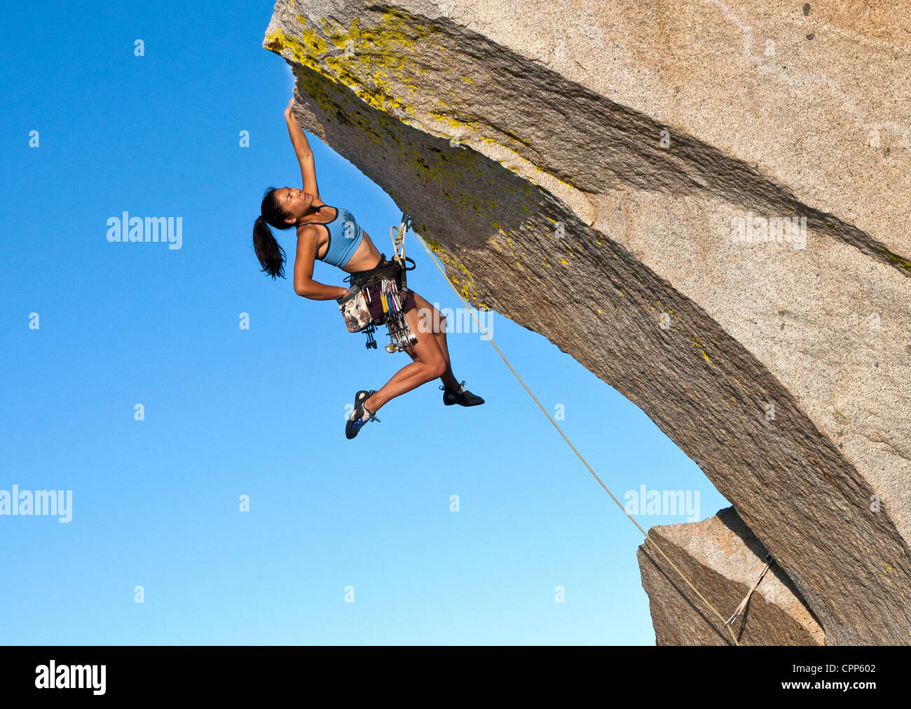 Female rock climber struggles to grip the edge of a challenging overhang. Stock Photo