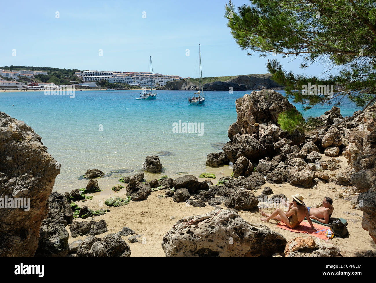 middle aged couple sunbathing amongst the rocks looking out into the bay of arenal d'en castell menorca balearic islands spain Stock Photo