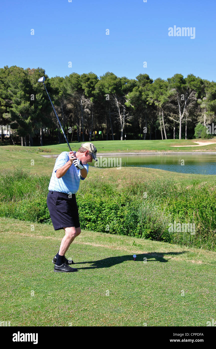 Male golfer hitting across lake on 8th hole at Golf Son Parc Golf Course, Son Parc, Menorca, Balearic Islands, Spain Stock Photo