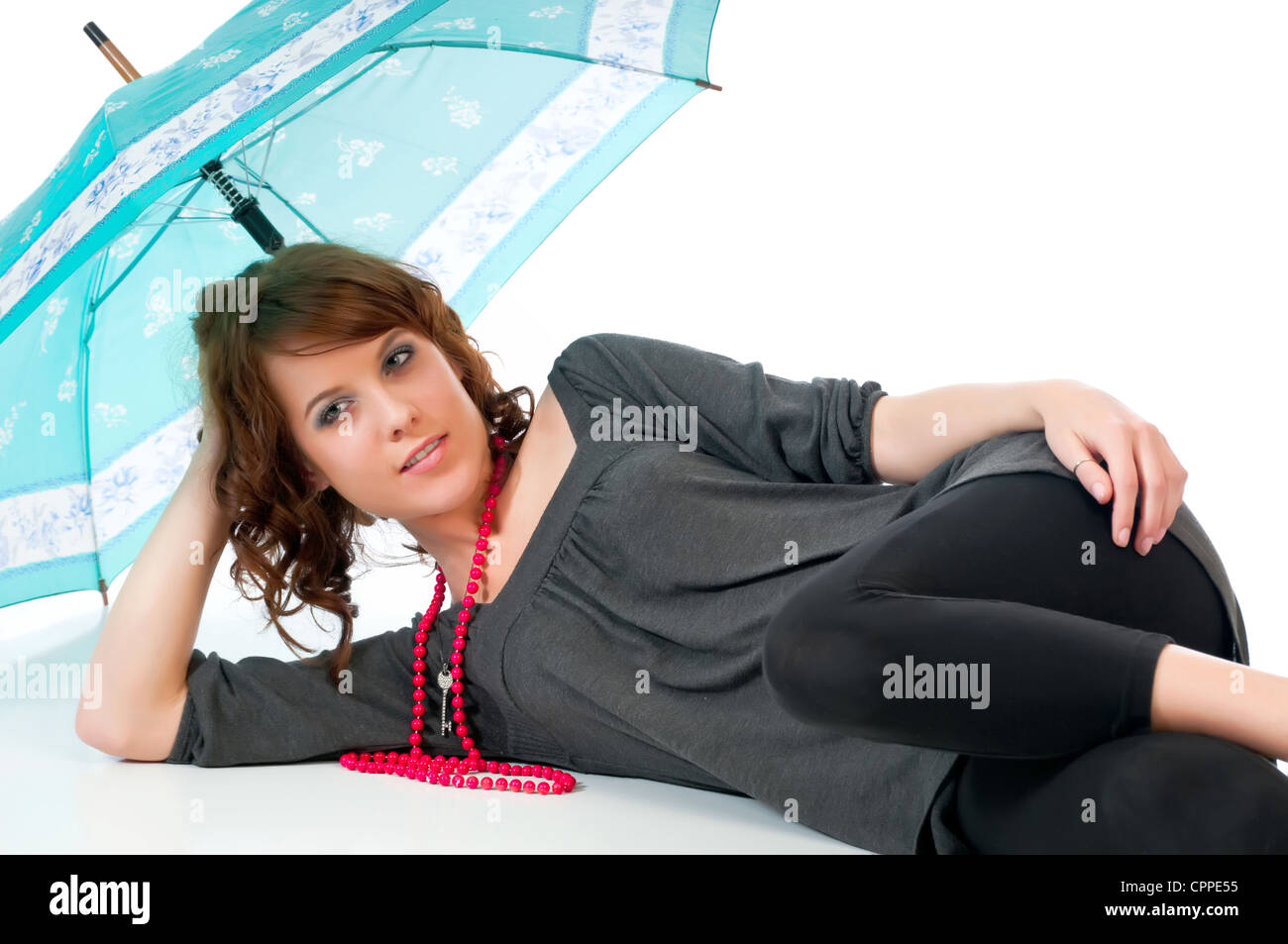 Beautiful young woman reclining under an umbrella against a white background and reflective floor. Stock Photo