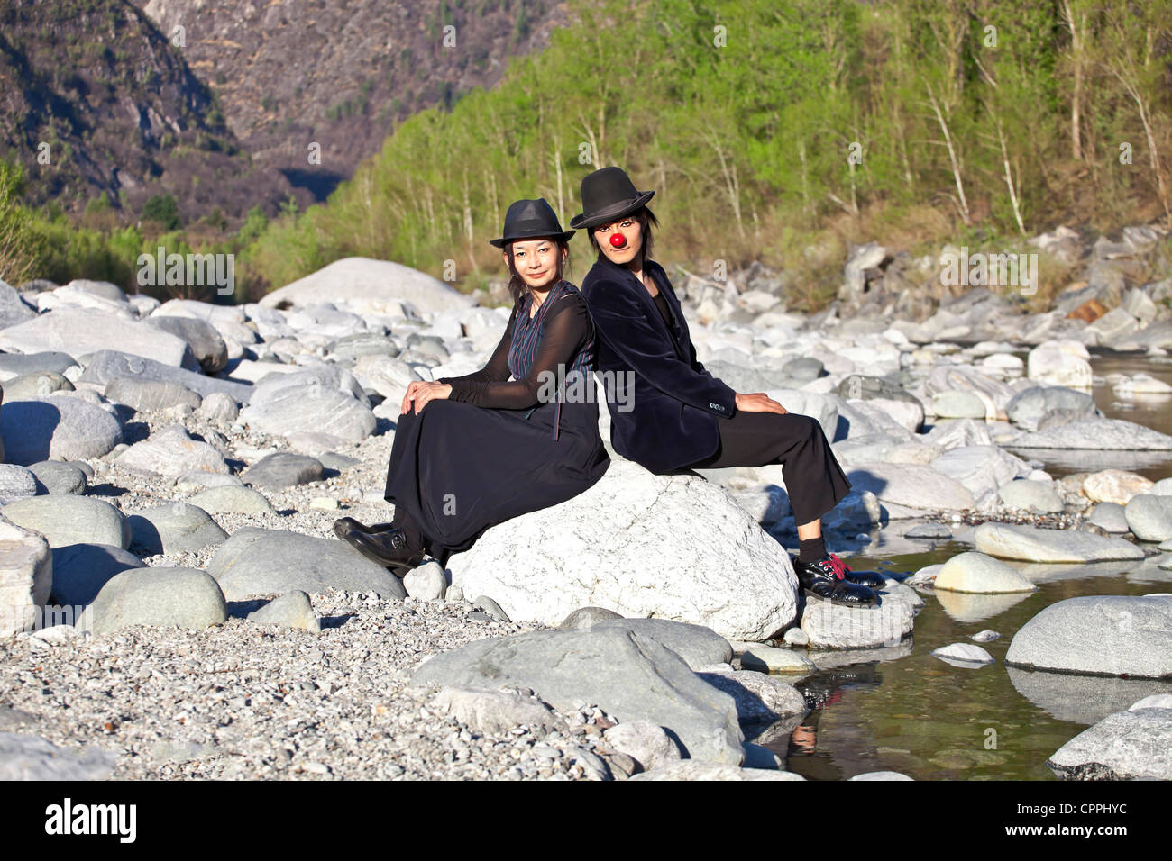 a clown couple sitting on a rock on the bank of a river Stock Photo