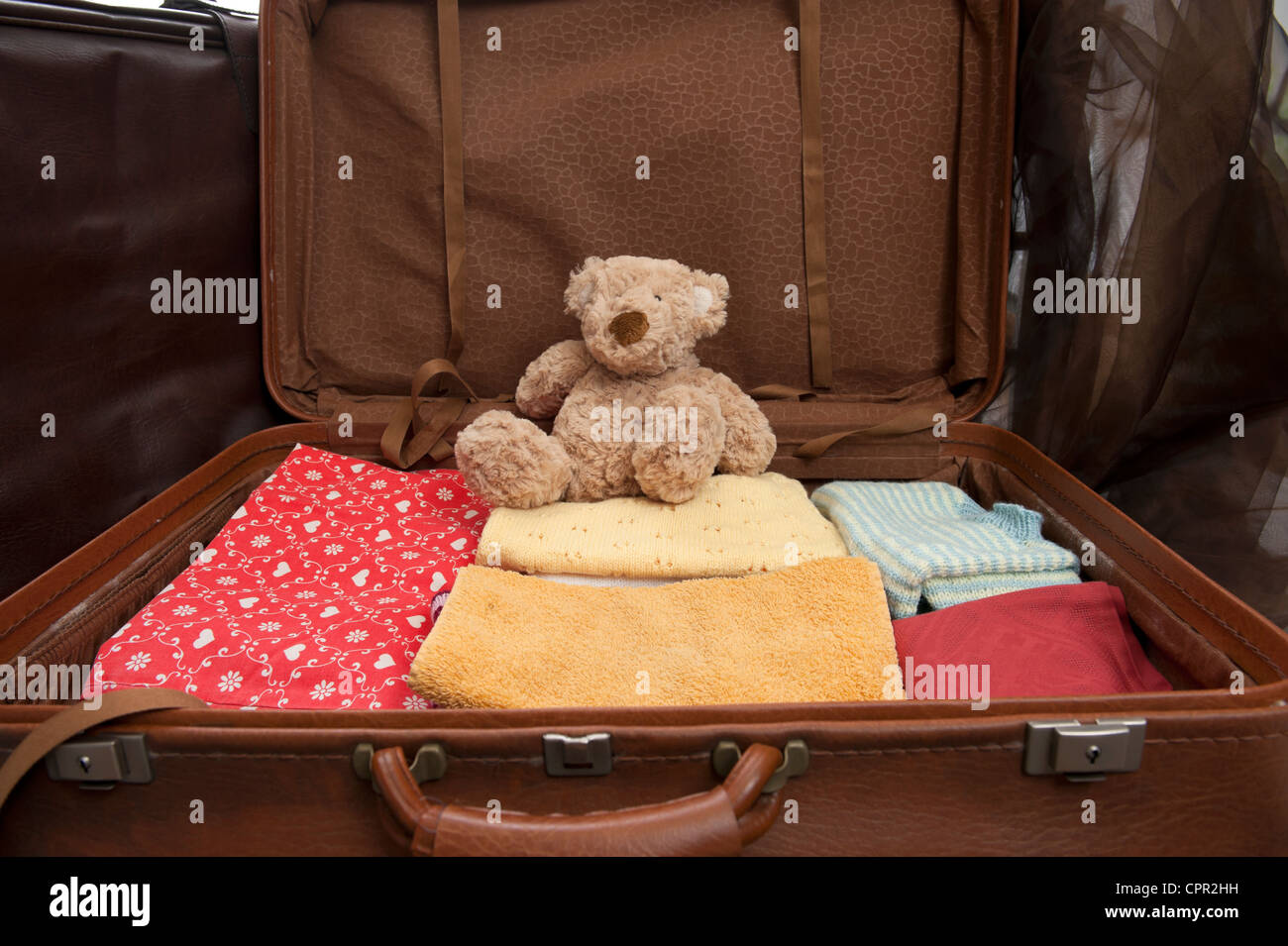 Open suitcase with clothes and teddy bear Stock Photo