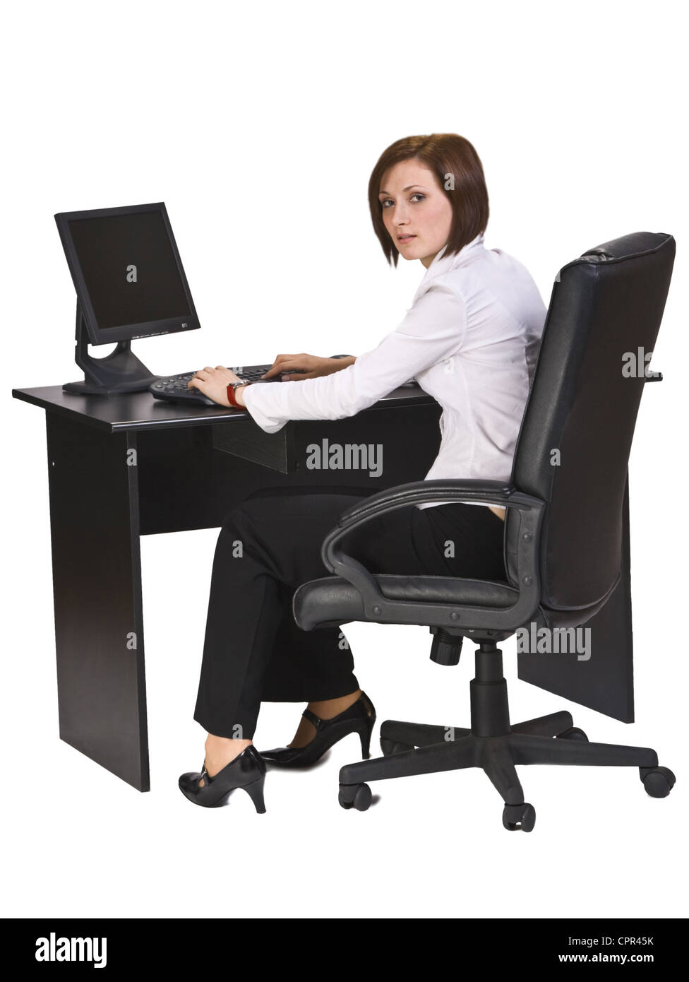 Young businesswoman at her desk working on the computer and looking back over the shoulder. Stock Photo