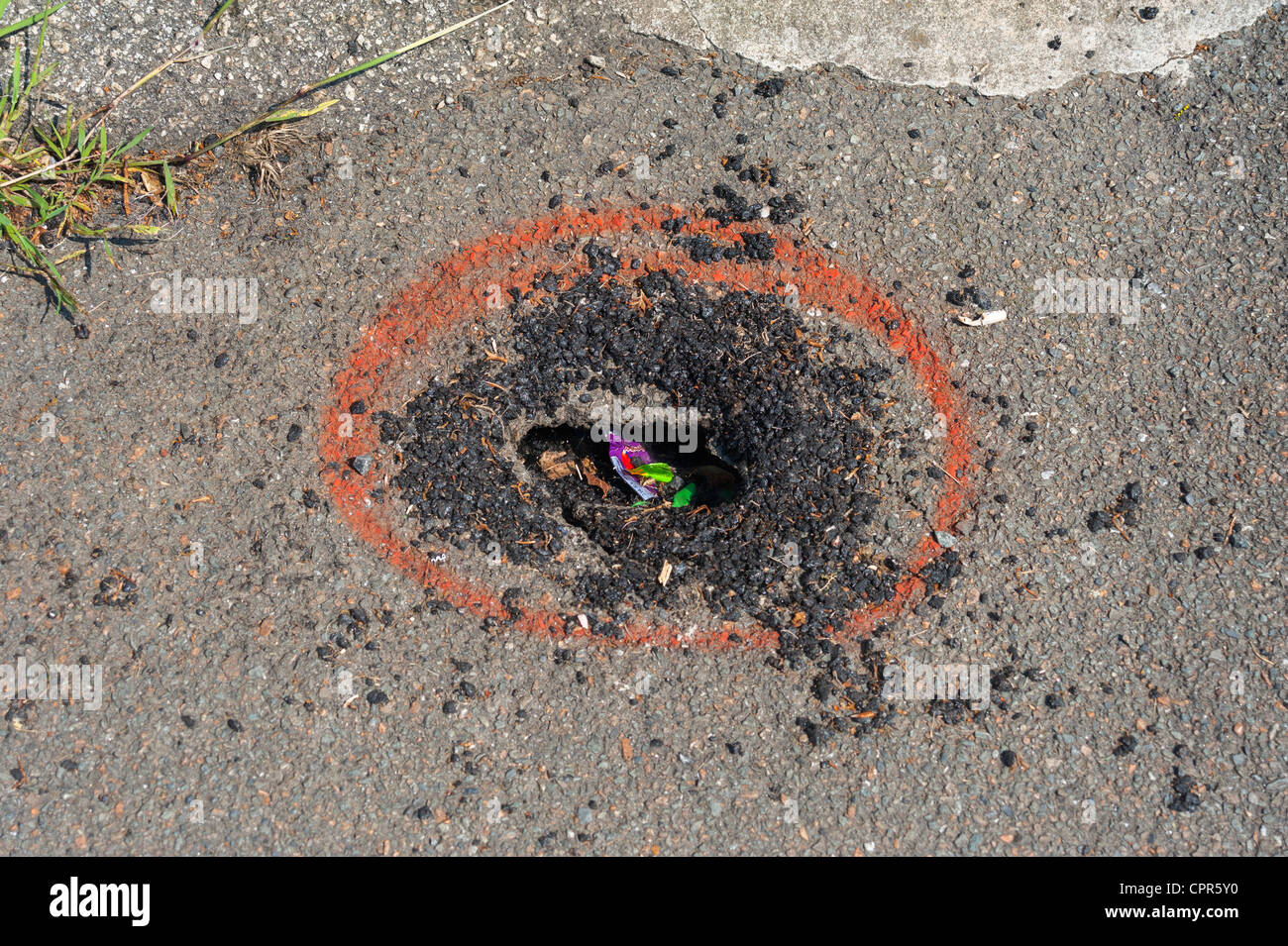A hole in a tarmac pavement with red circle to indicate. Stock Photo
