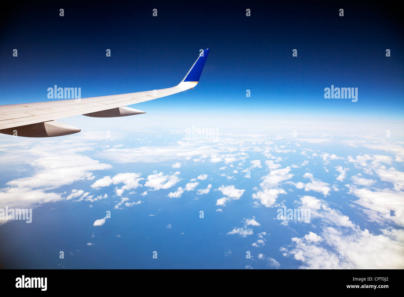 Looking out of the window of airplane out at the clouds and curvature of the earth and the wingtip of plane Stock Photo