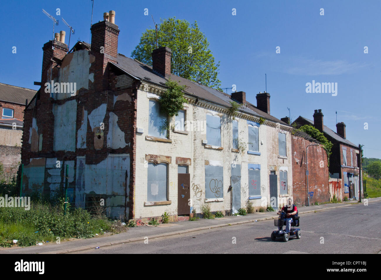 A man on a mobility scooter drives past a row of run down and abandoned derelict houses in Sheffield, South Yorkshire, England Stock Photo