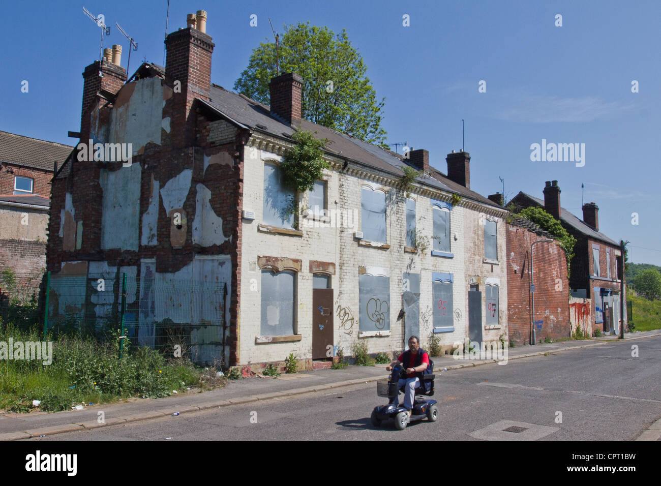 A man on a mobility scooter drives past a row of run down and abandoned derelict houses in Sheffield, South Yorkshire, England Stock Photo