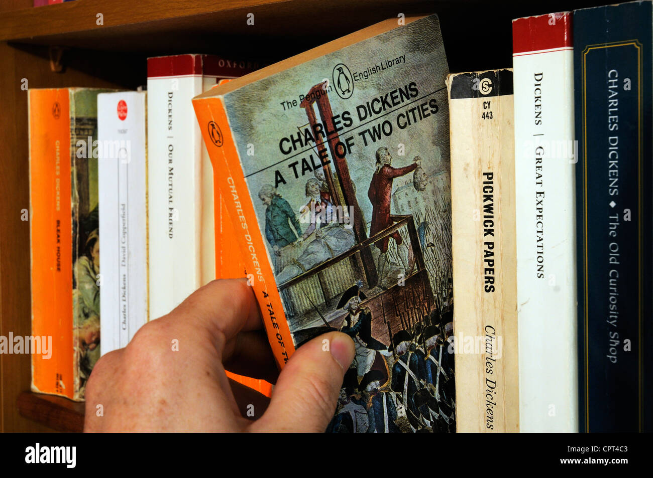 A hand taking Charles Dickens A Tale of Two Cities  from a bookshelf Stock Photo