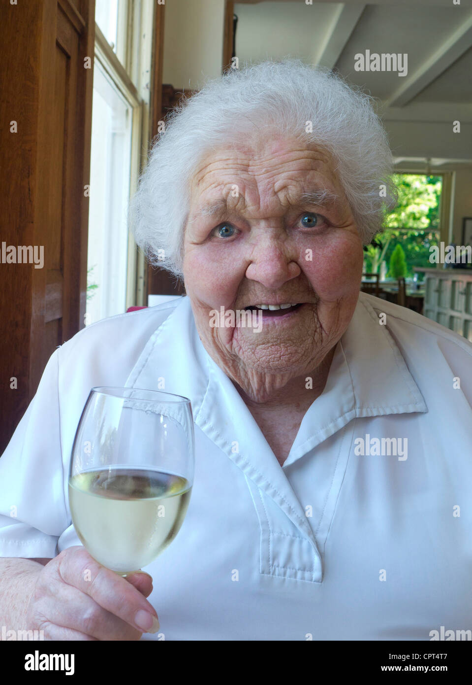 Happy elderly lady in her 90s enjoying a glass of white wine in large living room Stock Photo